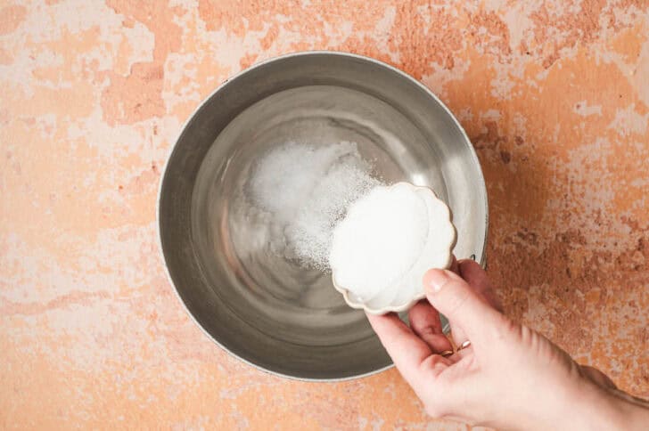A hand pouring sugar into a pot of water.
