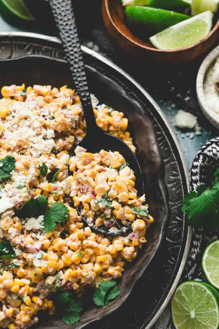 A bowl of elote salad recipe with a spoon digging into it.