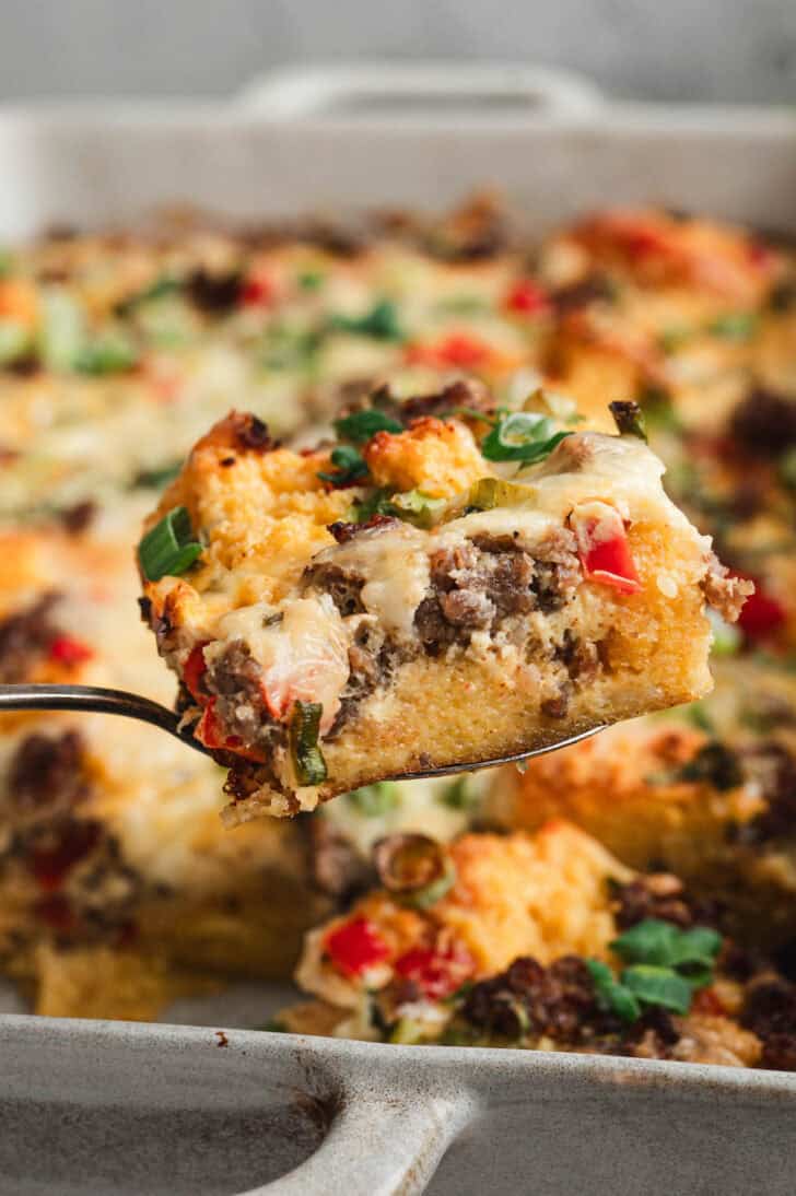 A server lifting a piece of leftover cornbread casserole from a baking dish.