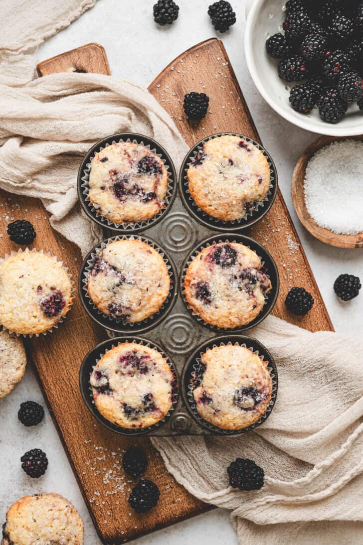 A pan of blackberry muffins on a wooden cutting board.