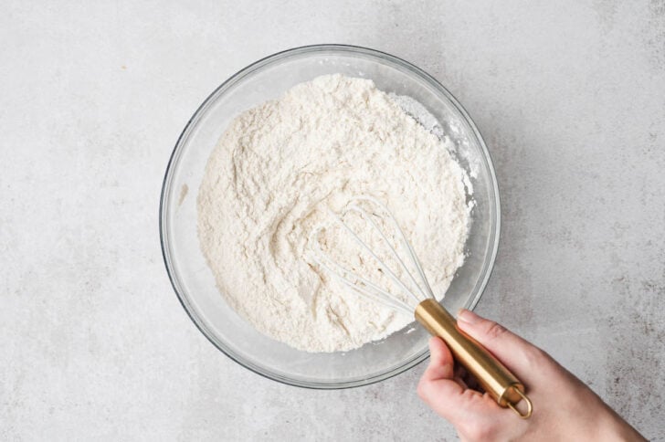 A hand whisking flour in a glass bowl.