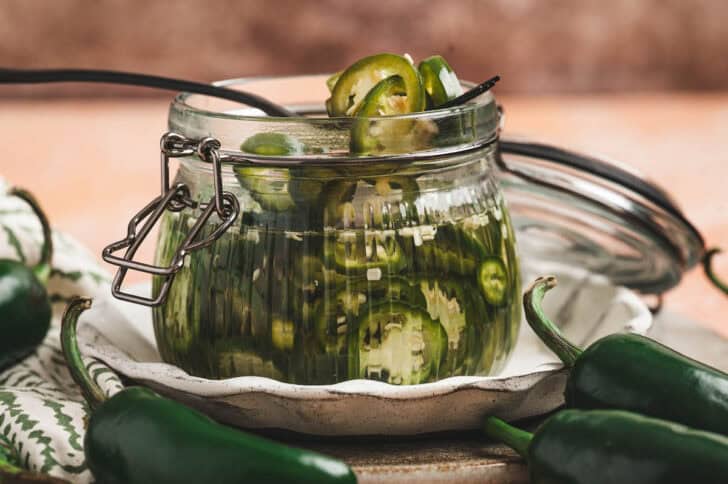 A fork lifting pickled jalapenos from a glass jar.