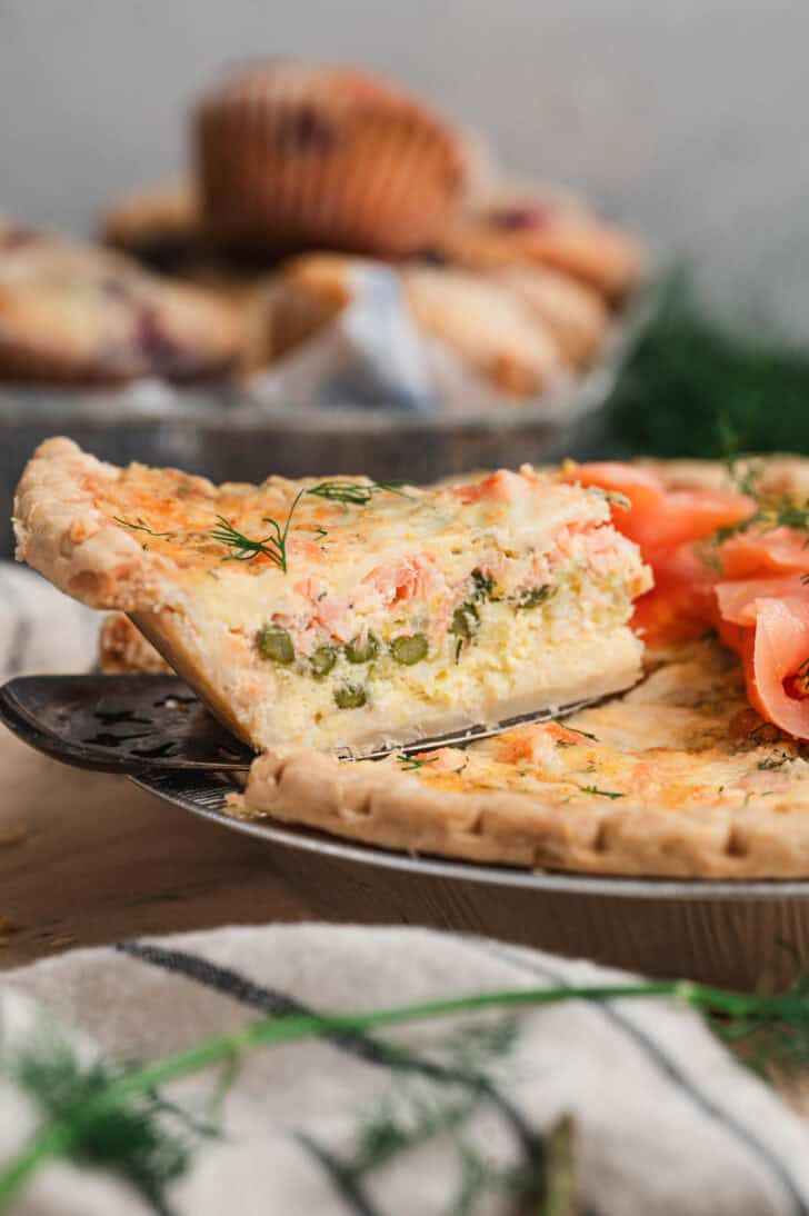 A pie server removing a slice of salmon quiche from a pan.