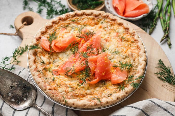 A smoked salmon quiche recipe being served on a wooden cutting board.