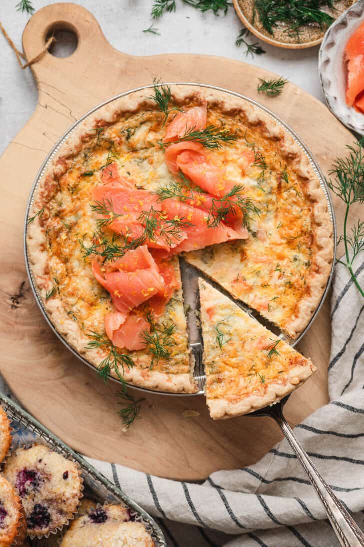 A salmon and asparagus quiche on a wooden board, with a slice being removed from it.