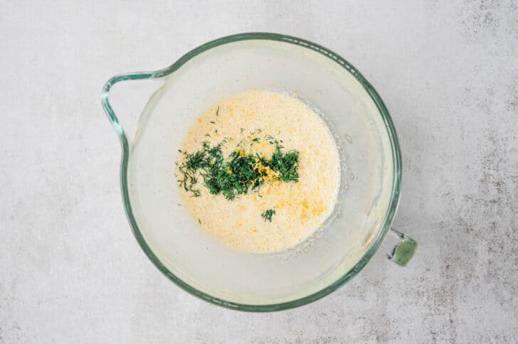 Whisked eggs and chopped herbs in a glass mixing bowl.
