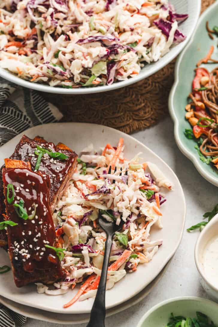 A plate with ribs and a serving of apple cider vinegar slaw, with a fork digging in.