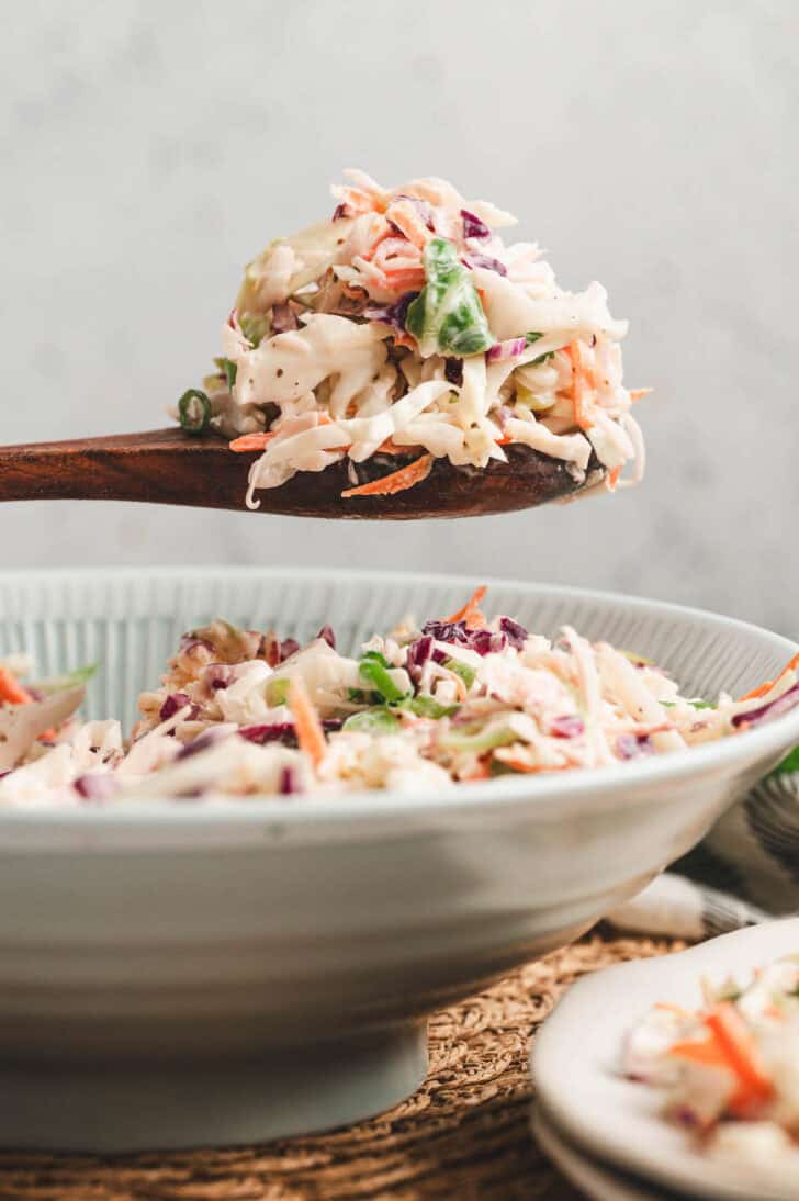 A wooden spoon lifting a scoop of apple cider slaw from a bowl.