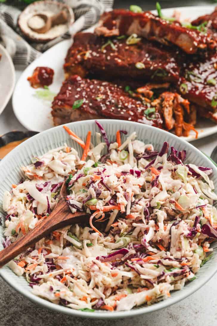 A bowl of celery seed slaw in front of a platter of ribs.