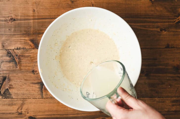 Water being poured into a creamy dressing in a white bowl.