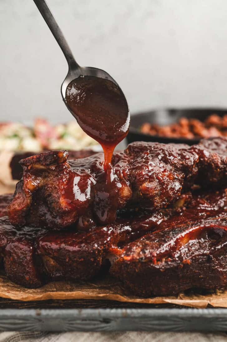 A spoon drizzling barbecue sauce over country pork ribs.
