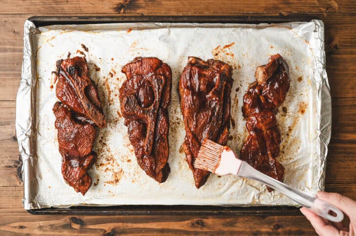 A silicone brush brushing sauce on country style pork ribs in oven.