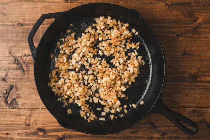 Chopped onions cooking in a cast iron skillet.