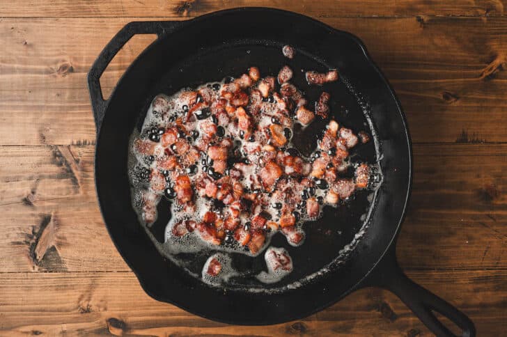 Chopped bacon cooking in a cast iron skillet.