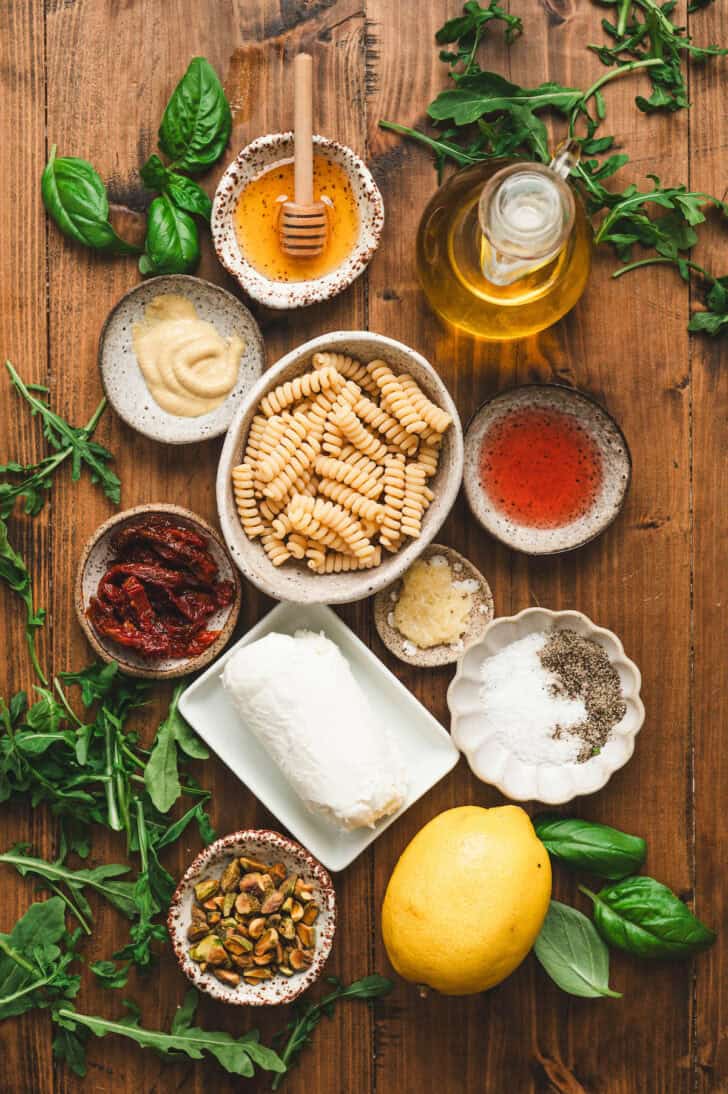 Ingredients on a wooden background, including pasta, goat cheese, lemon, garlic, honey, herbs and spices.