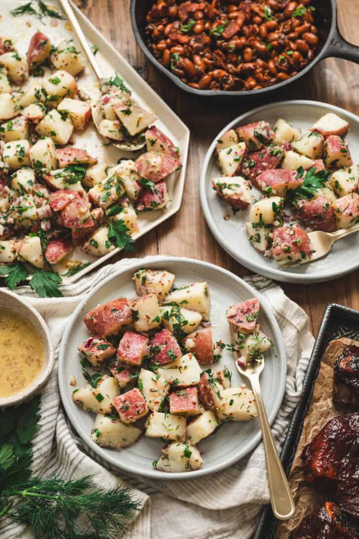 Two plates filled with vinaigrette potato salad, alongside a bowl of baked beans.