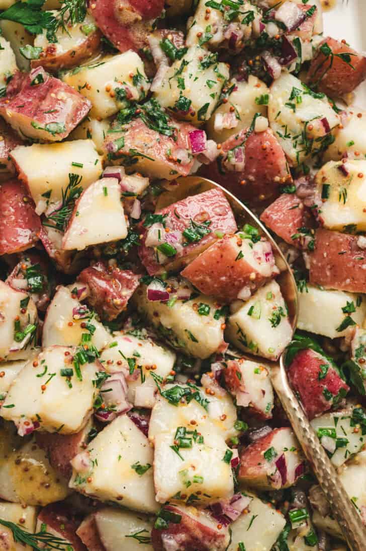 A no mayo potato salad recipe with a spoon in it.