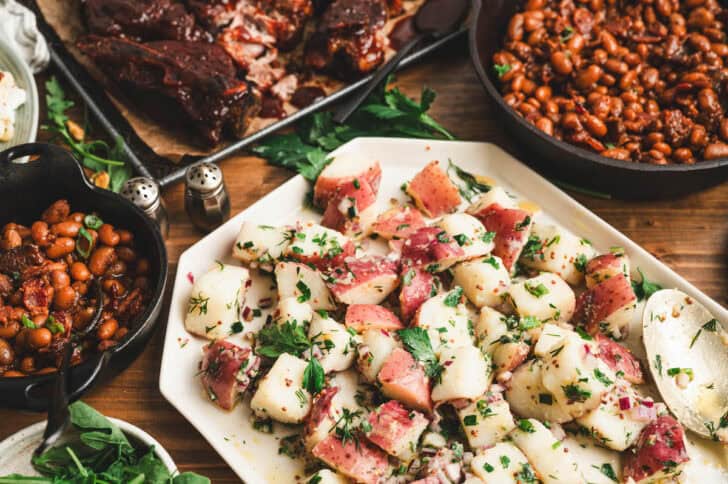 A platter of herb potato salad, with ribs and baked beans in the background.