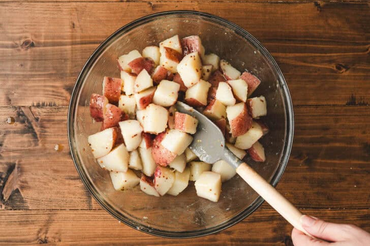 Potato salad without mayonnaise being stirred together in a glass bowl.