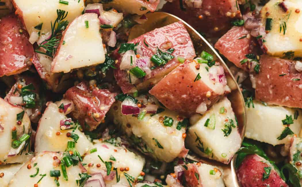 A no mayo potato salad recipe with a spoon in it.