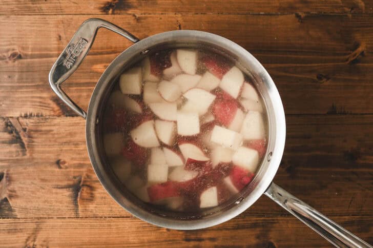 Quartered red potatoes being boiled in a pot of water.