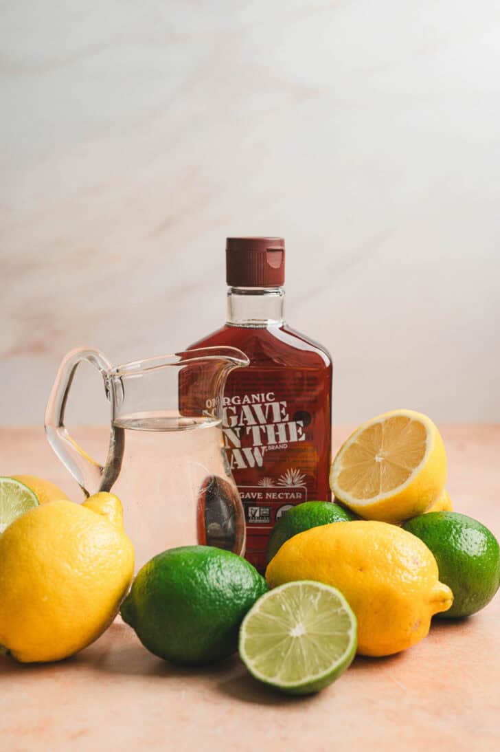 Ingredients on a light background, including lemons, limes, and agave nectar.