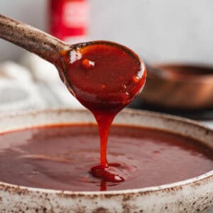 A spoon drizzling Asian BBQ sauce into a bowl.