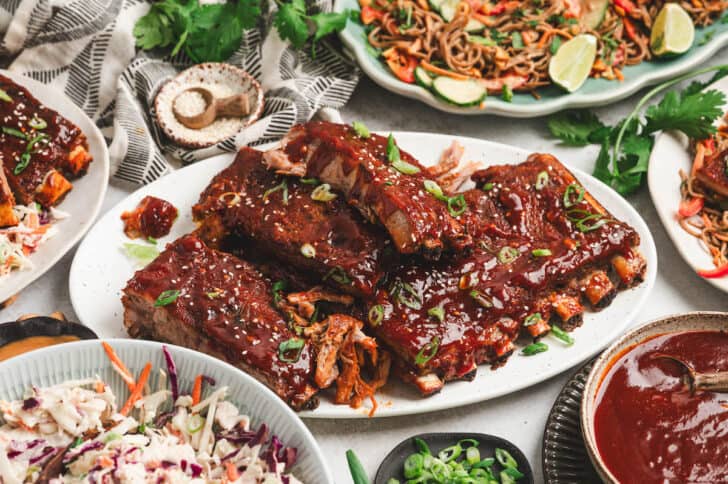 A platter of Asian BBQ spare ribs with side dishes all around it.