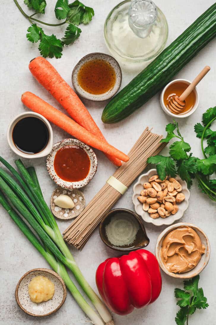 Ingredients on a white background, including soba noodles, vegetables, peanuts, herbs and spices.