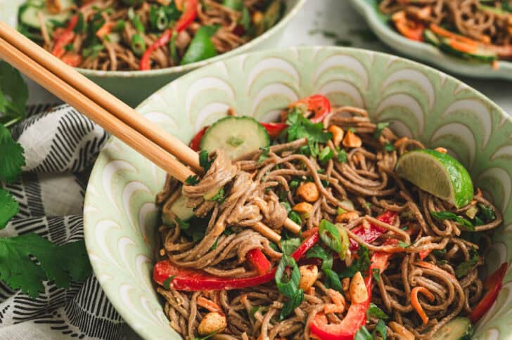 A bowl filled with an Asian noodle salad recipe, with chopstick taking a bite.
