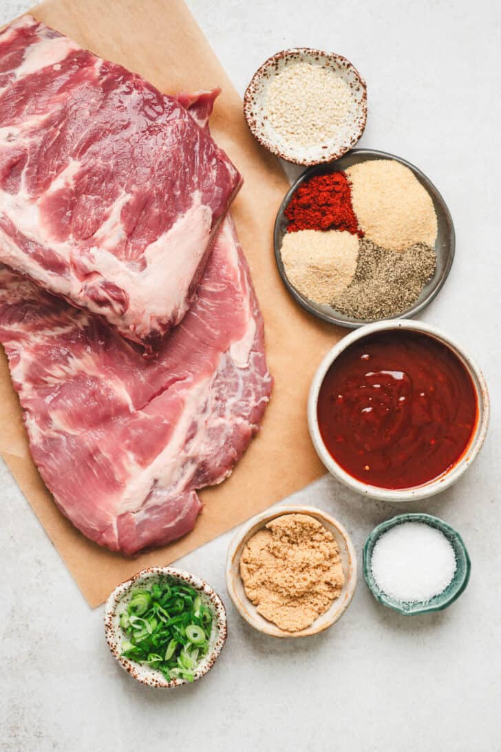 Ingredients on a white background, including raw pork, barbecue sauce, sesame seeds, green onions, and spices.