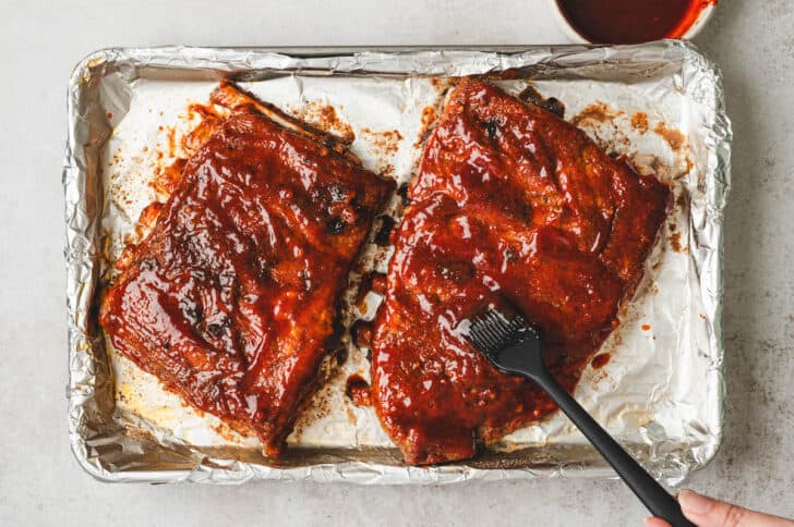 An Asian ribs recipe being brushed with sauce on a baking pan.