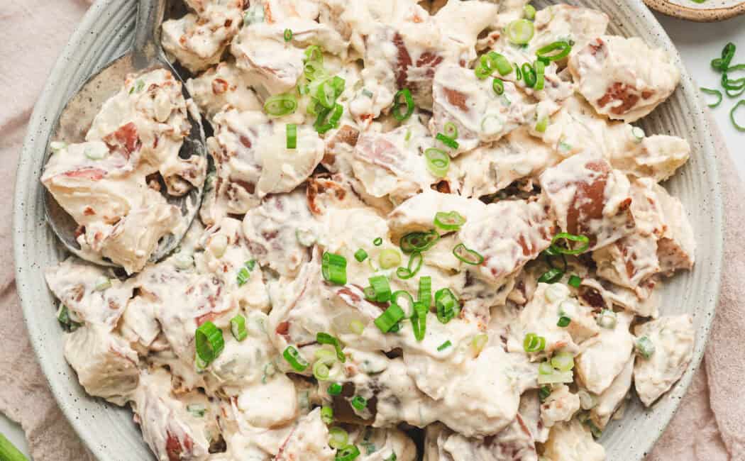 A white bowl filled with potato salad with bacon.