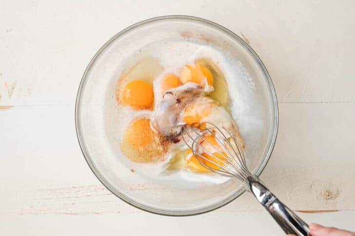 Eggs, milk and spices being whisked in a glass bowl.