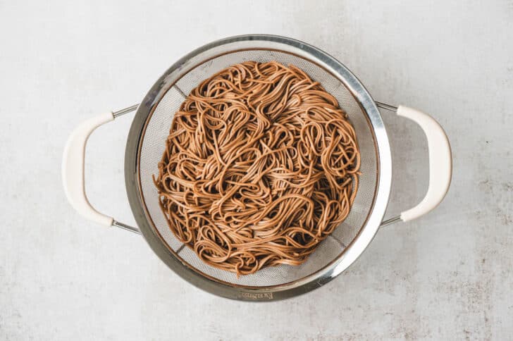 A colander filled with cooked soba noodles.