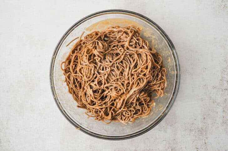 A glass bowl filled with soba noodles tossed in peanut dressing.
