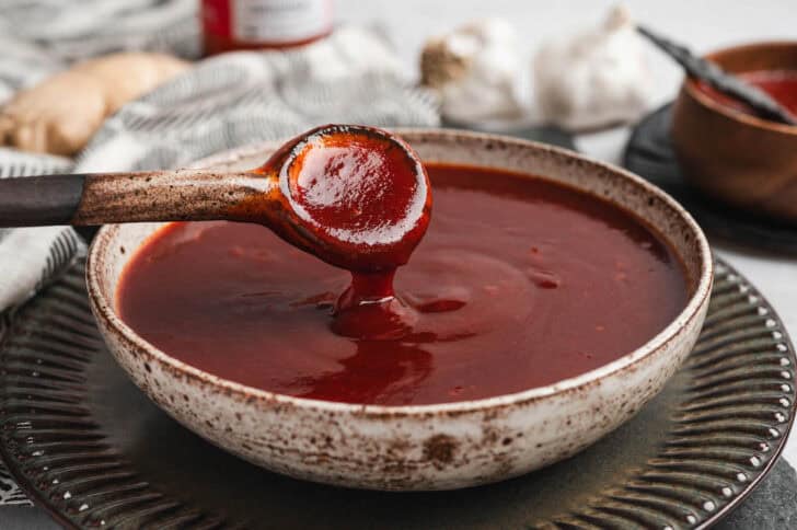 A spoon drizzling a gochujang bbq sauce recipe into a bowl.