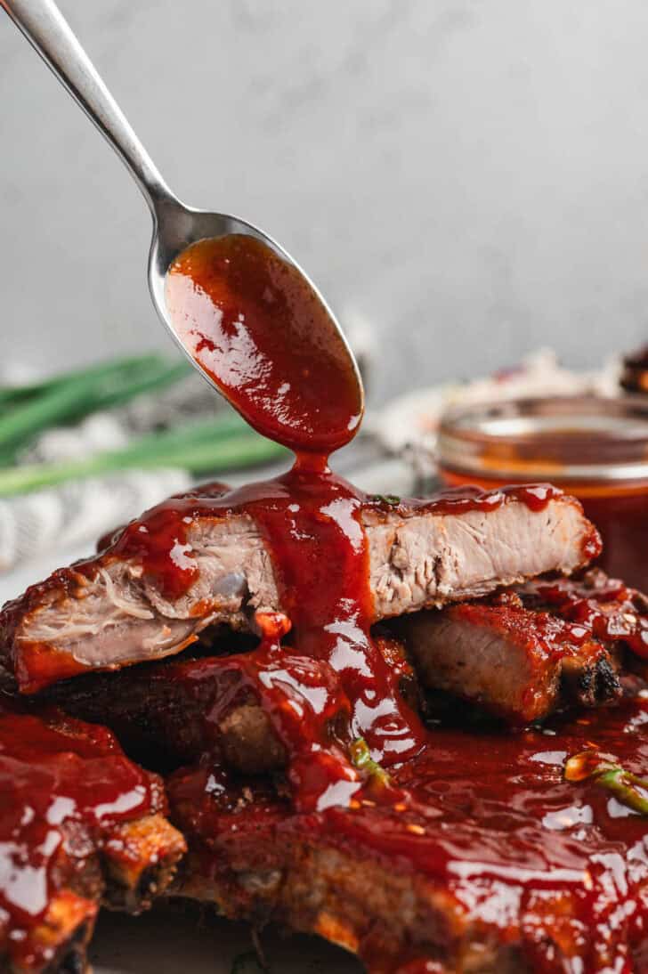 A spoon drizzling Asian BBQ sauce over ribs.