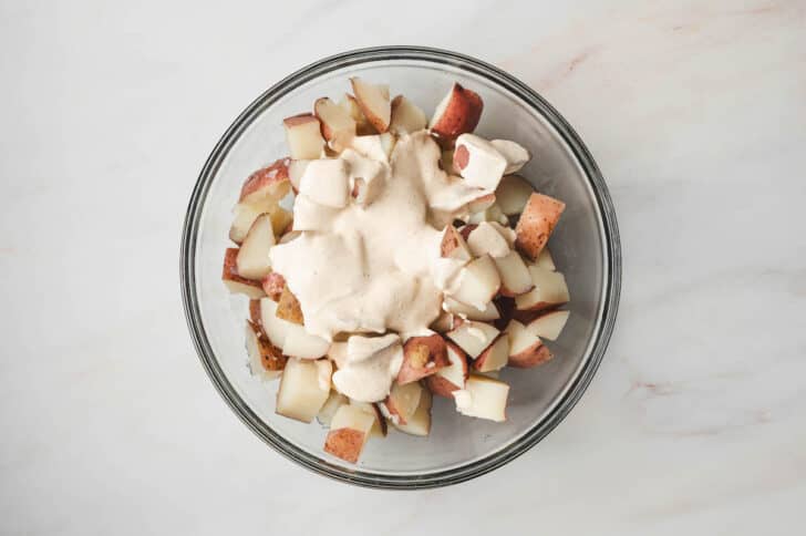 Chopped cooked red potatoes with creamy dressing poured over them.