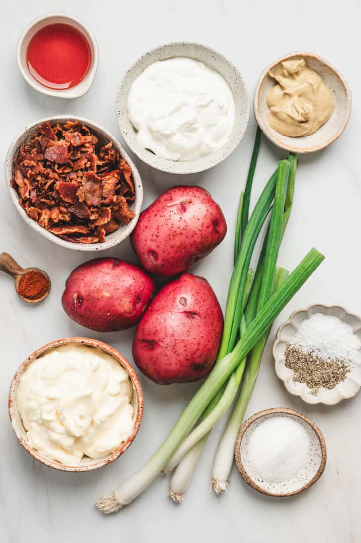 Ingredients on a light background, including redskin potatoes, green onions, mayonnaise, mustard, bacon and spices.