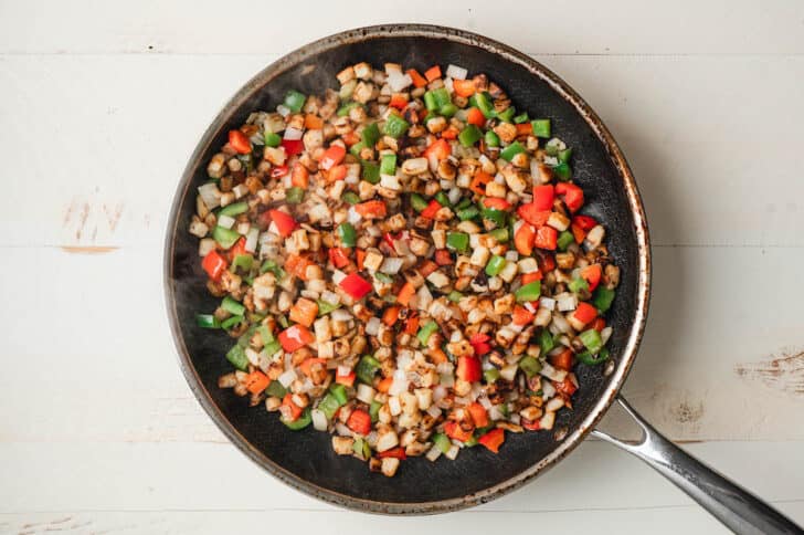 Cubed potatoes, bell peppers and onions being cooked in a skillet.