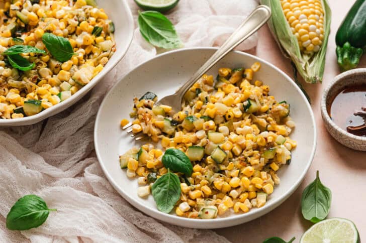 A shallow white bowl filled with a corn and zucchini recipe.