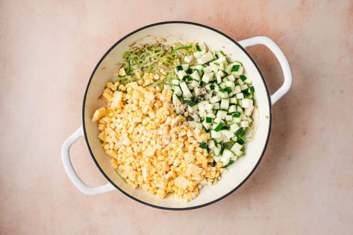 Thinly sliced leeks, corn kernels and diced zucchini in a white skillet.