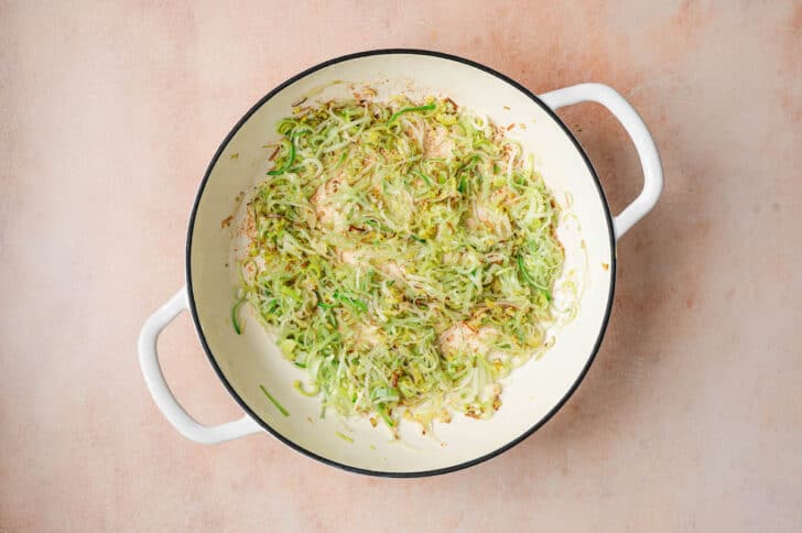 A white skillet with handles, with thinly sliced leeks being sauteed in it.