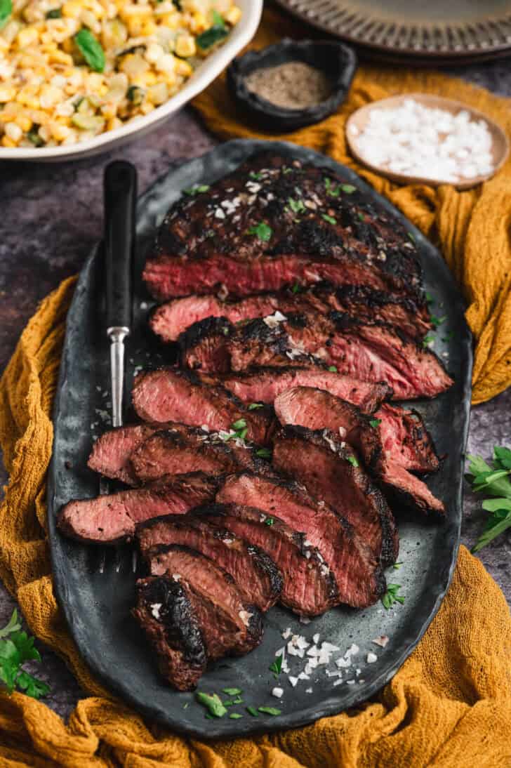 Marinated flat iron steak, cooked and thinly sliced, on a platter.
