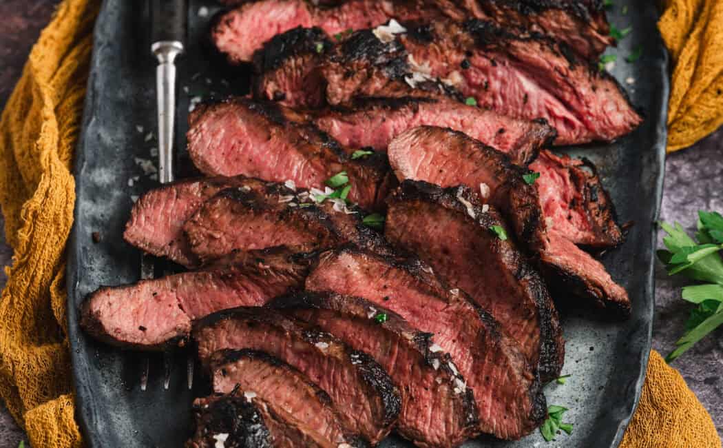 Marinated flat iron steak, cooked and thinly sliced, on a platter.