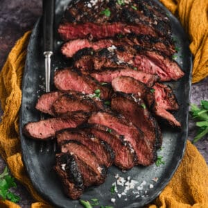 Marinated flat iron steak, cooked and thinly sliced, on a platter.