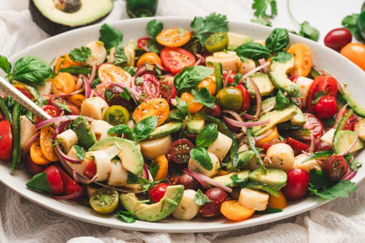 Hearts of palm and avocado salad with tomatoes, red onion, herbs and jalapeno arranged on a serving platter.