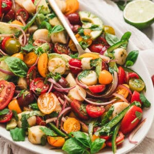 Heart of palm salad recipe with avocado, cherry tomatoes, red onion, basil, cilantro and jalapeno served on a platter with lime wedges.