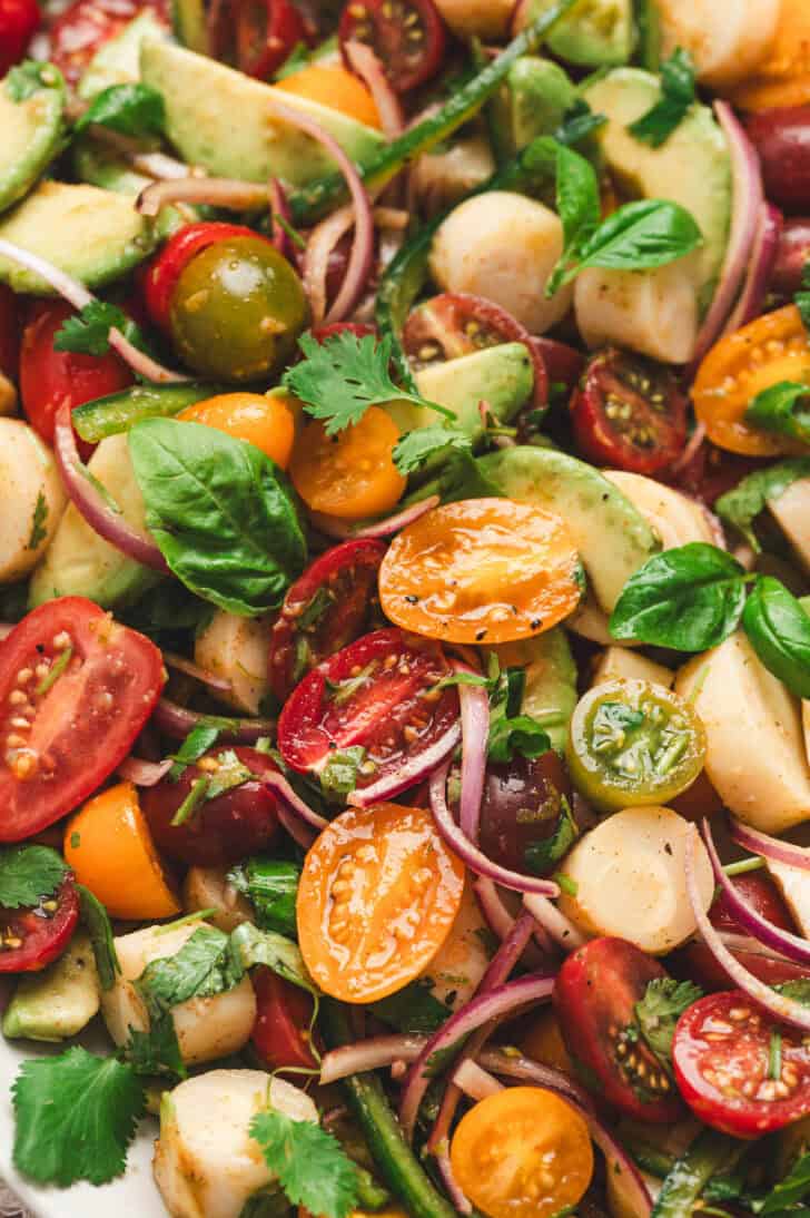 Hearts of palm salad with avocado, tomatoes, herbs and jalapeno served on a white platter with fresh basil and cilantro.